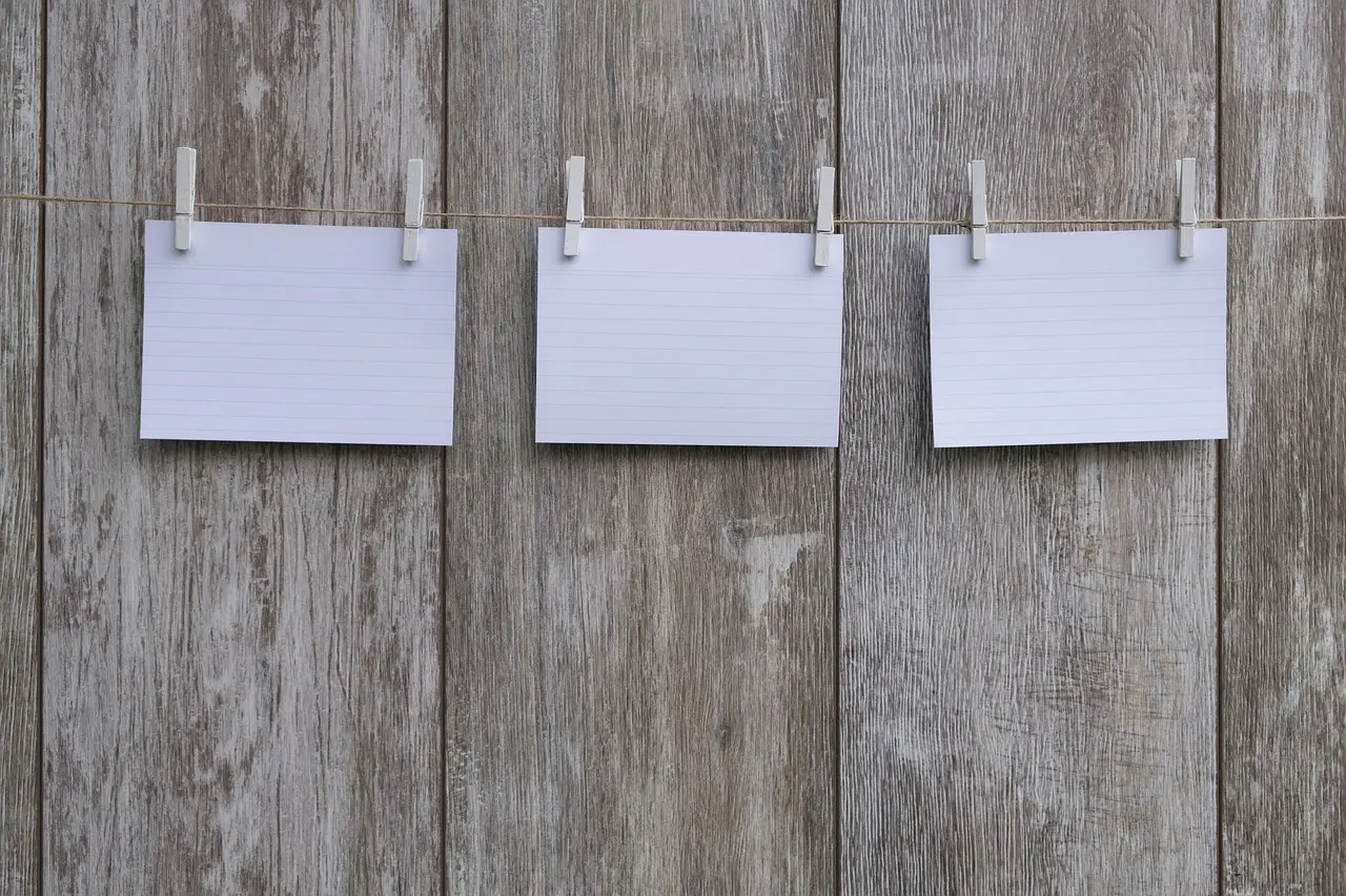 Three blank cards pegged on a string against a wooden wall